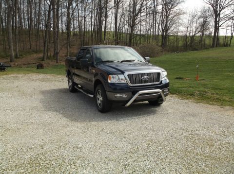 2005 Ford F-150 - This dark blue 2005 Ford F-150 pickup truck is parked on a gravel driveway with a wooded area in the background.
