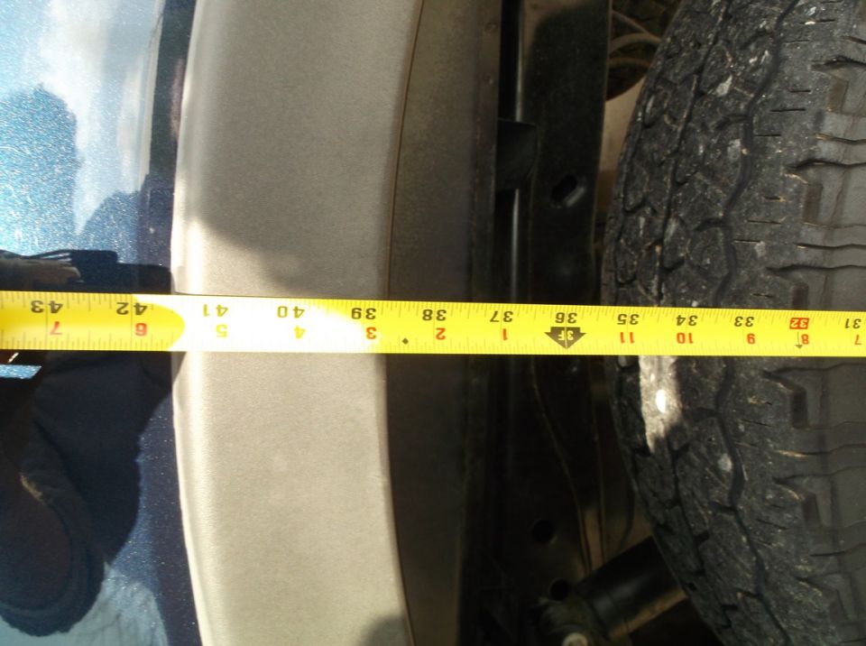 Close-up of a tire and fender well with a yellow measuring tape