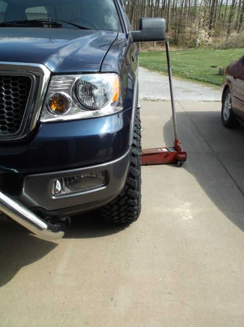 2005 Ford F-150 - A blue Ford F-150's front wheel is visible as it is being lifted by a red hydraulic jack.
