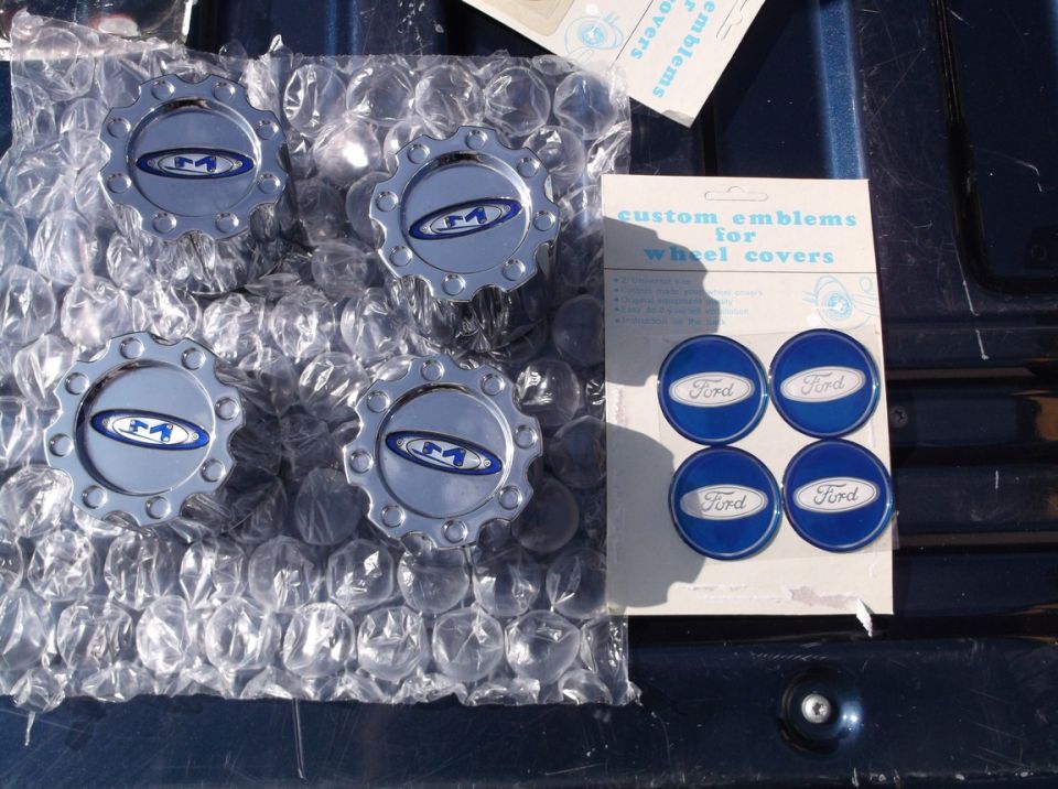 Four chrome wheel center caps with blue and silver emblems, and a package of four blue Ford emblems