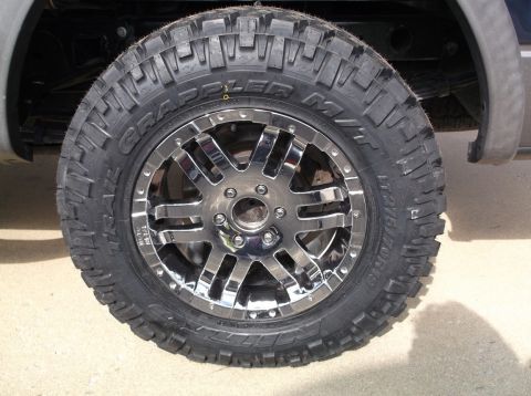 2005 Ford F-150 - Close-up of a vehicle's wheel and tire assembly, showing custom chrome rims and off-road tires.