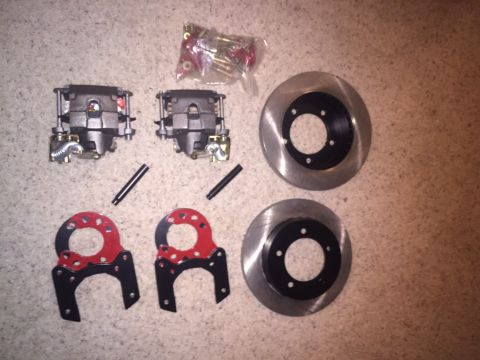 1982 Ford Bronco - A set of brake calipers, rotors, and hardware are laid out on a carpeted surface.