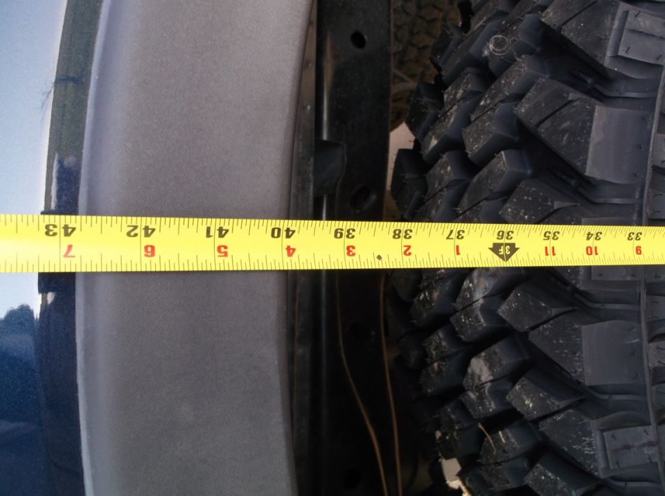 Yellow measuring tape against a tire and vehicle body panel, showing clearance