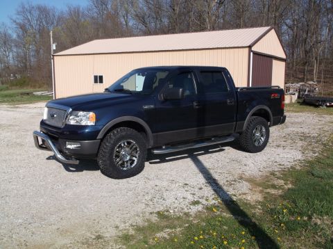 2005 Ford F-150 - This dark blue Ford F-150 pickup truck is shown from a 3/4 front angle, parked in front of a metal building.