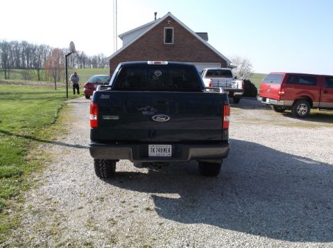 2005 Ford F-150 - A dark-colored Ford F-150 pickup truck is parked in a gravel driveway with other vehicles and a house in the background.