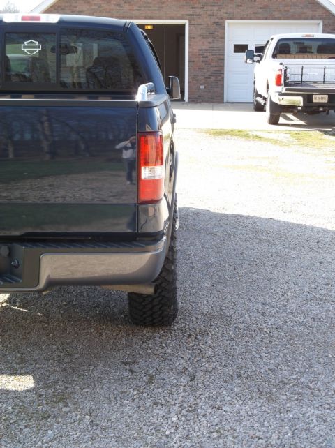 2005 Ford F-150 - A dark pickup truck is parked in a gravel driveway next to a white pickup truck.