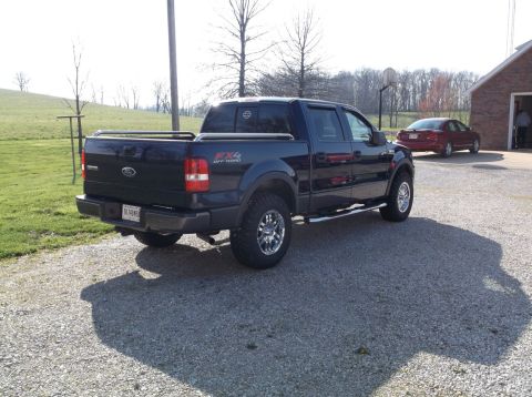 2005 Ford F-150 - Dark blue Ford F-150 pickup truck with FX4 Off Road badging is parked on gravel, with a red sedan in the background.
