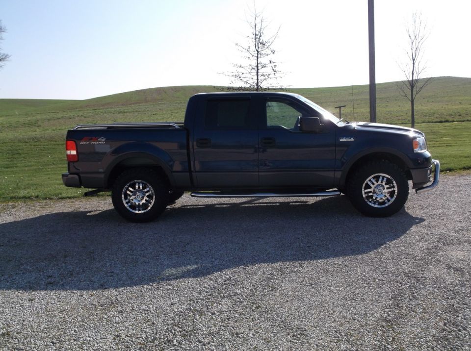 Dark blue Ford F-150 pickup truck, side view, aftermarket wheels, chrome side steps, tonneau cover