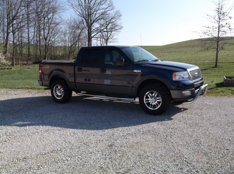 2005 Ford F-150 - Dark blue 2005 Ford F-150 pickup truck parked on a gravel driveway with a rural background.