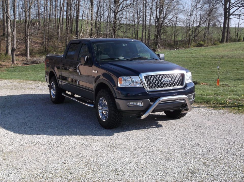 Dark blue 2005 Ford F-150 pickup truck parked on gravel with trees in background