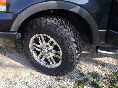 2005 Ford F-150 - Close-up of a truck's wheel and fender, a chrome rim and aggressive tire tread.