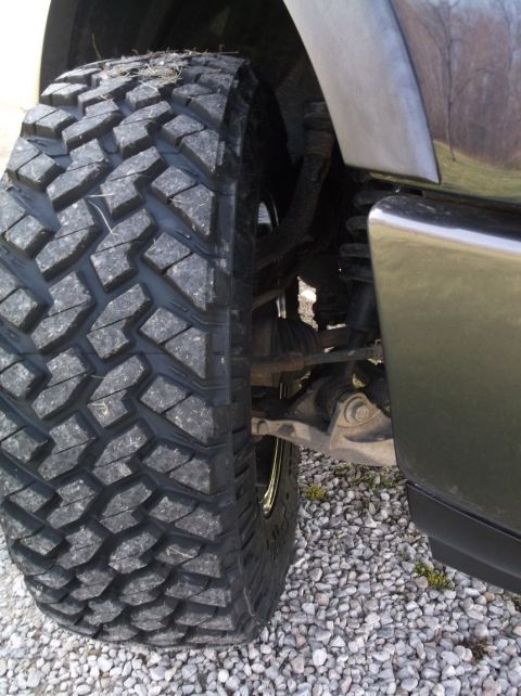 2005 Ford F-150 - A close-up view of a vehicle's tire and suspension system, with gravel on the ground.