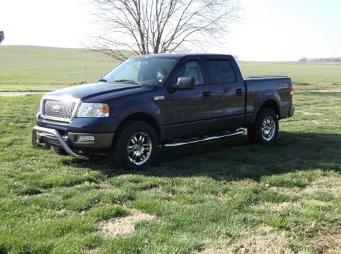 2005 Ford F-150 - A dark blue 2005 Ford F-150 pickup truck is shown from a 3/4 front view, a chrome grille guard and aftermarket wheels.