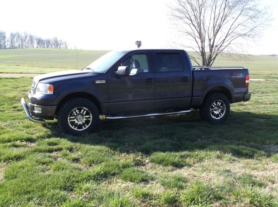 Dark blue 2005 Ford F-150 crew cab pickup truck parked on grass with aftermarket wheels and a chrome bull bar