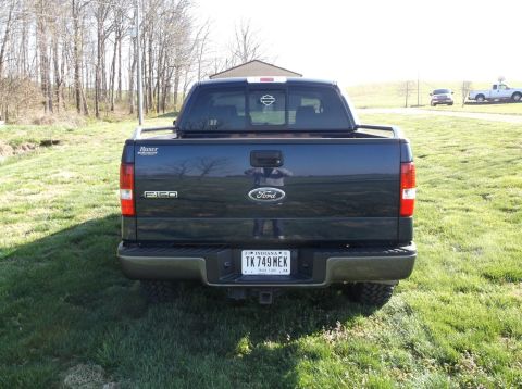 2005 Ford F-150 - Dark blue Ford F-150 pickup truck parked in a grassy field. Another truck is in the background.