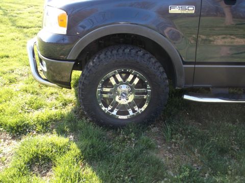 2005 Ford F-150 - A dark blue Ford F-150 truck's front wheel and fender are visible, with a chrome bull bar and running board.