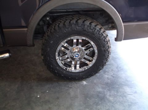 2005 Ford F-150 - Close-up of a chrome wheel and aggressive off-road tire installed on a dark blue truck, likely a 2005 Ford F-150.
