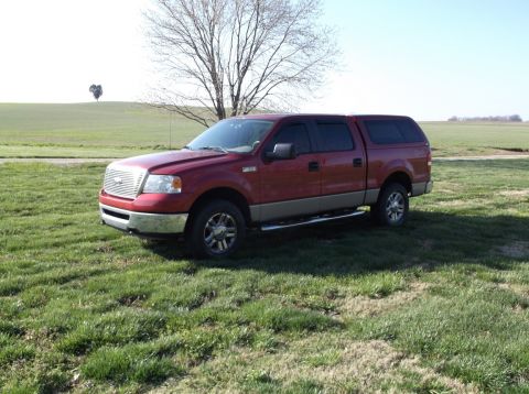 2005 Ford F-150 - Red 2005 Ford F-150 pickup truck with a tan lower body and a cap, parked in a grassy field.