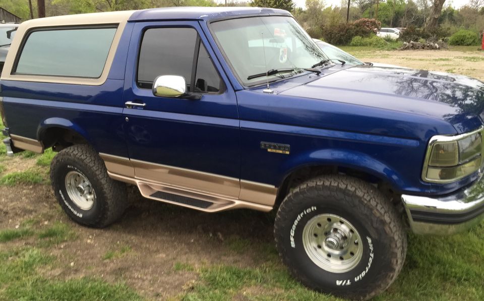 Blue Ford Bronco with tan trim and running boards, parked on grass