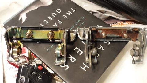 1976 Ford Ranchero - A pair of car door handles, one in good condition and the other showing signs of rust, are laid out on a book.