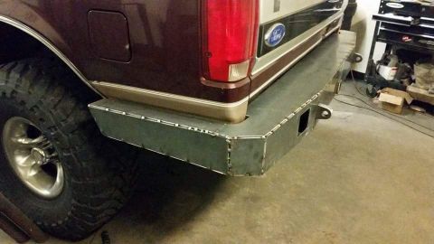 1996 Ford Bronco - The rear of a maroon Ford Bronco shows a custom-welded metal bumper and a large off-road tire.