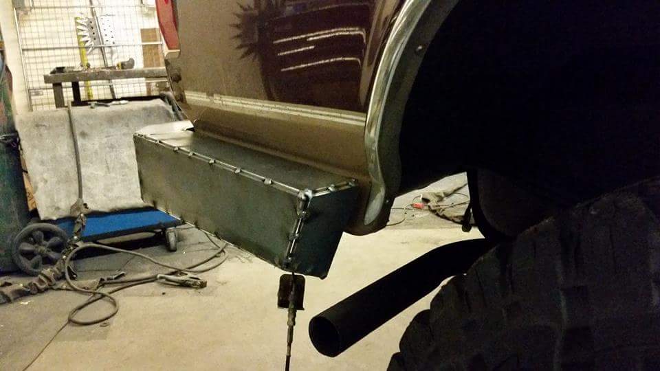 Custom metal step bumper with visible welds, attached to a dark brown vehicle. Exhaust pipe visible
