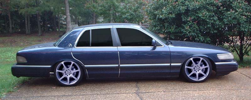 Dark blue lowered Mercury Grand Marquis sedan with large aftermarket wheels, side view on a driveway