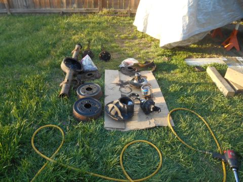 1972 Ford Bronco - Various vehicle parts, including an axle and brake drums, are laid out on the grass next to an air tool.