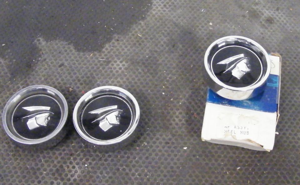 Three chrome hubcaps with black centers showing the Mercury Cougar emblem, one on a box