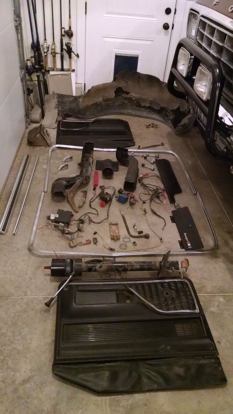 1979 Ford F-150 - Vehicle parts and fishing rods are laid out on a garage floor, with a partial vehicle visible in the background.