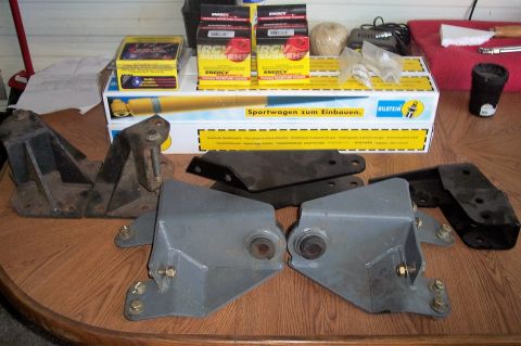 1990 Ford Bronco - Various suspension parts and a Bilstein shock absorber box are laid out on a wooden table.