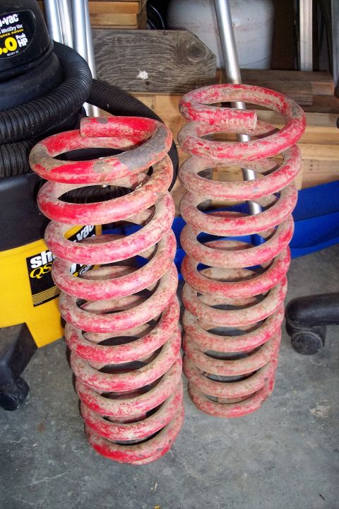 1990 Ford Bronco - Two red coil springs are shown, likely for a vehicle suspension system, with a shop vac in the background.