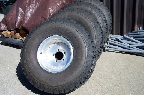 1990 Ford Bronco - Four off-road tires and rims are visible, with a tarp and firewood in the background.