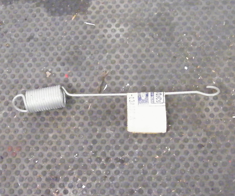 Metal spring with a white tag attached, lying on a textured gray surface