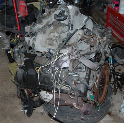 1985 Mercury Grand Marquis - Engine assembly with chains attached, resting on a tire. "SUPERMOTORS" logo visible.