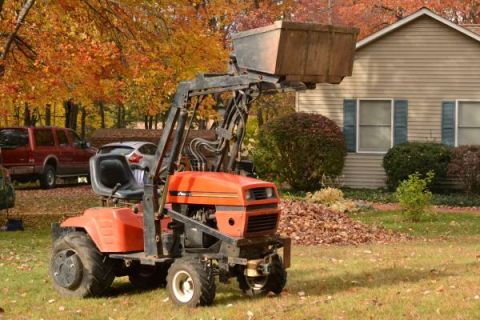 1982 Kubota RTV900 - A tractor with a front loader sits in a yard with fall foliage and a house in the background.