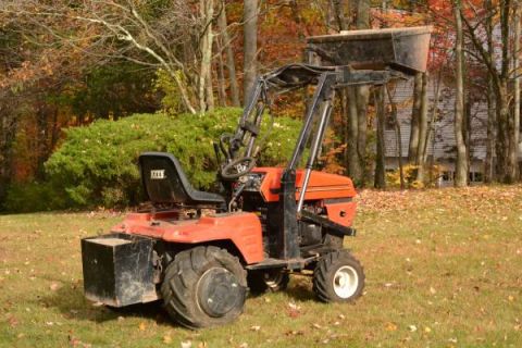 1982 Kubota RTV900 - An orange tractor with a front loader attachment sits on a lawn during autumn.
