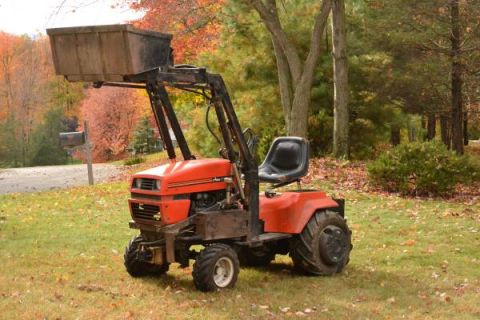 1982 Kubota RTV900 - An orange tractor with a front loader is parked on a lawn surrounded by trees in autumn.