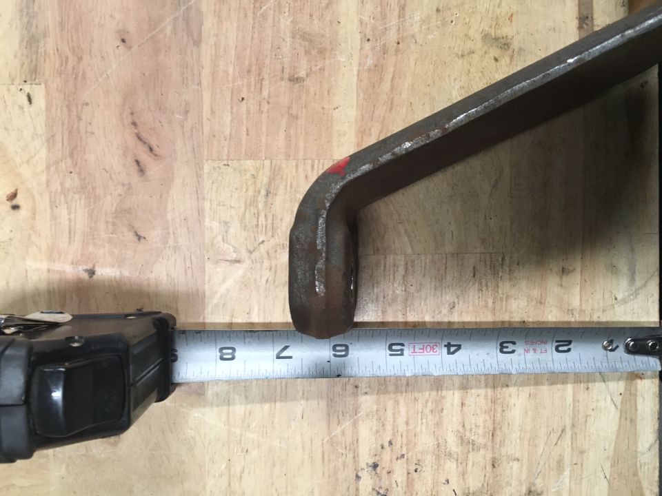 Metal drop pitman arm with red paint mark, measured with a tape measure on a wooden surface