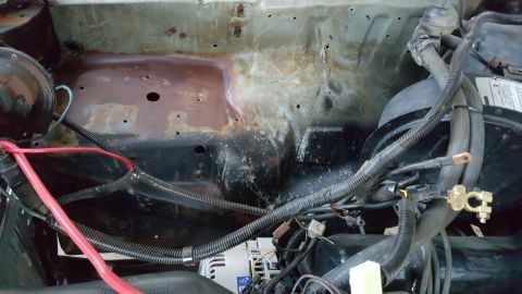 1978 Ford Bronco - The engine bay of a 1978 Ford Bronco shows a rusty firewall with various electrical components and hoses. A red battery cable is prominentl…