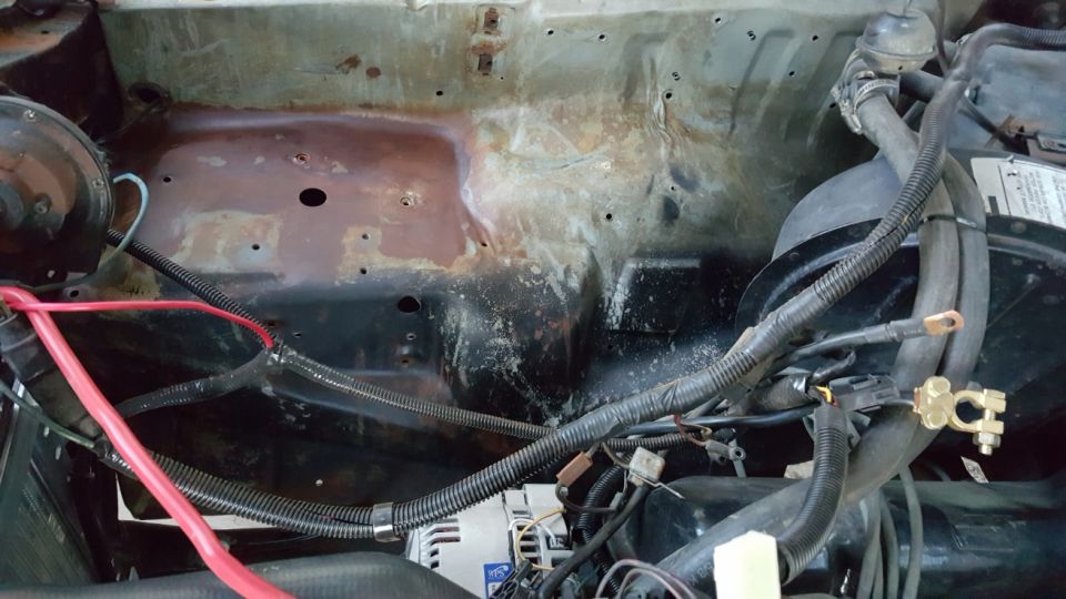 1978 Ford Bronco engine bay with rusty firewall, electrical wires, and red battery cable.