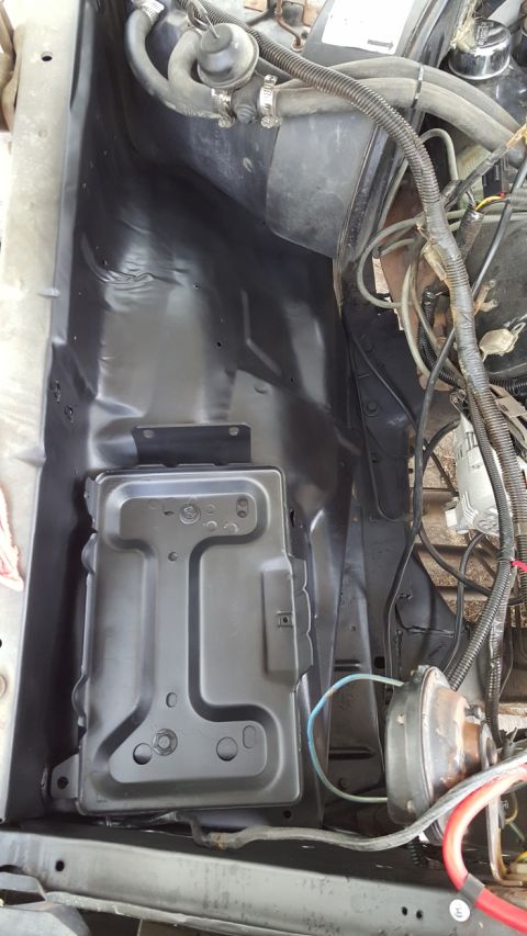 1978 Ford Bronco - A black painted battery tray is mounted in the engine bay of a vehicle, with various hoses and wiring visible around it.