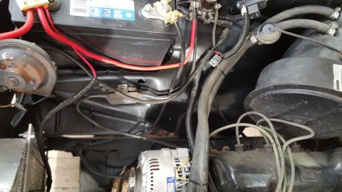 1978 Ford Bronco - The engine bay of a 1978 Ford Bronco features a black battery, red battery cables, and an alternator. Various hoses and wiring are visible…