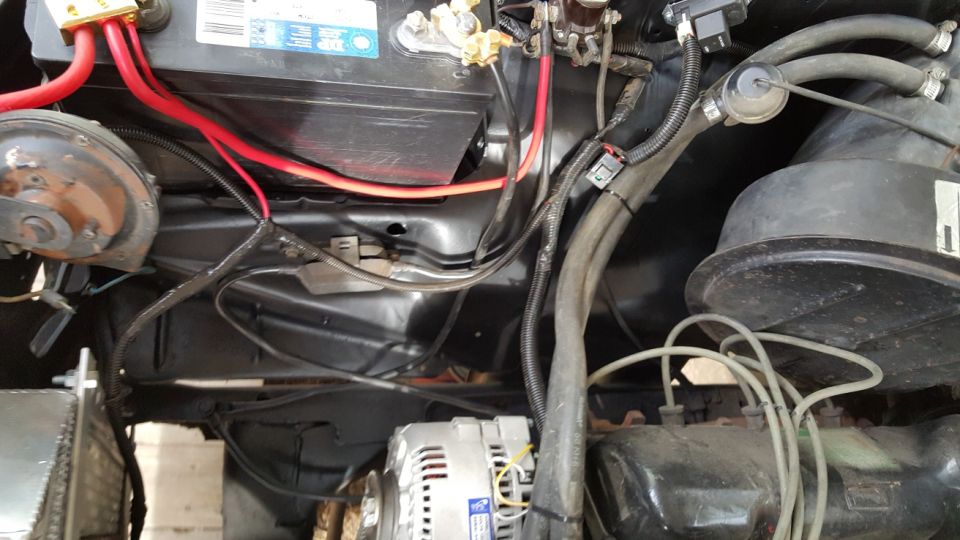 1978 Ford Bronco engine bay with battery, alternator, hoses, and wiring.