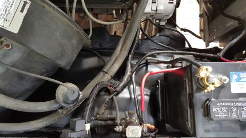 1978 Ford Bronco - This is a close-up view of the engine bay of a 1978 Ford Bronco, focusing on the battery, alternator, and various hoses and wiring. The bat…