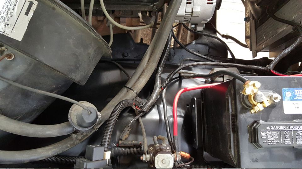 1978 Ford Bronco engine bay with battery, alternator, and wiring.