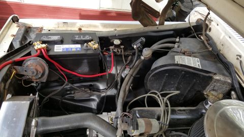 1978 Ford Bronco - The engine bay of a vintage Ford Bronco shows a black battery with red cables connected to a horn and other components. The engine compartm…