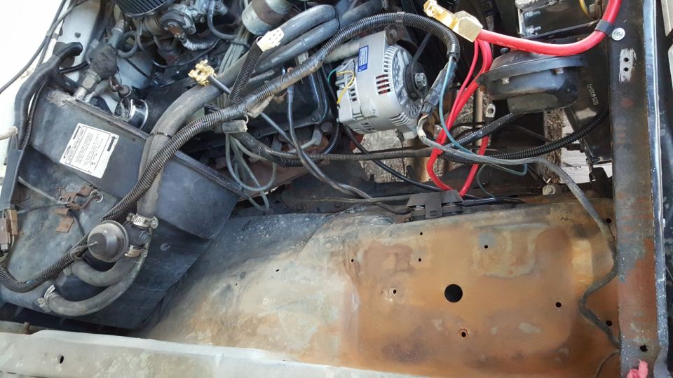 Engine bay of a 1978 Ford Bronco with alternator, hoses, and rusty frame.