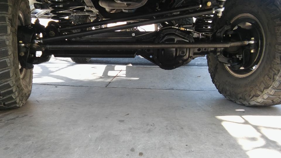 Underside of a lifted 4x4 vehicle showing steering linkage, differential, and suspension.