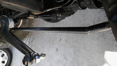1979 Ford Bronco - A close-up view of the underside of a vehicle, focusing on the steering linkage. The linkage appears to be a heavy-duty tie rod, possibly m…